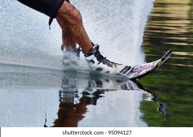 A close up of a slalom water skiers legs on a wake board with water splash.