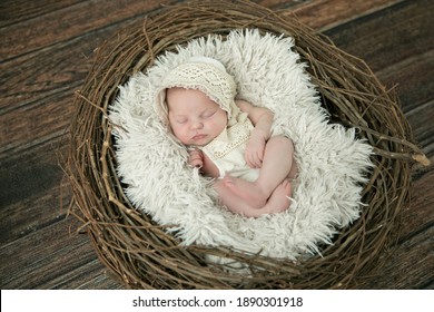 Close Up Of A Sleeping Sweet Newborn Infant Baby Girl With A Cream-colored Bonnet Hat On Laying On A Pale Neutral Background Laying In A Basket Wreath