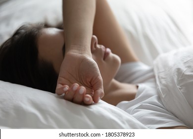 Close up sleepless young woman lying in bed, suffering from insomnia, tired exhausted female covering face with hand, trying to sleep, resting under white warm duvet on soft pillow - Powered by Shutterstock