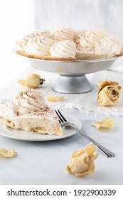 Close Up Of A Slice Of Banana Cream Pie With The Pie In Behind And Dried Roses For Decoration.