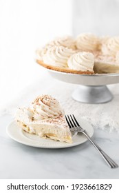 Close Up Of A Slice Of Banana Cream Pie With The Full Pie In Behind Against A Bright Sunny Window.