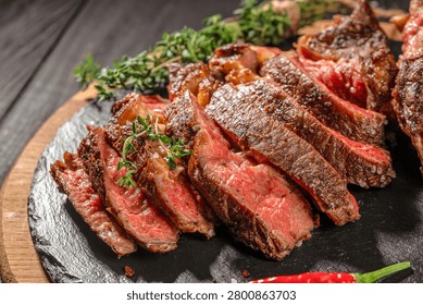 Close up of sliced medium rare tomahawk steak with thyme and sea salt on slate serving board. Juicy grilled beef with visible texture.
