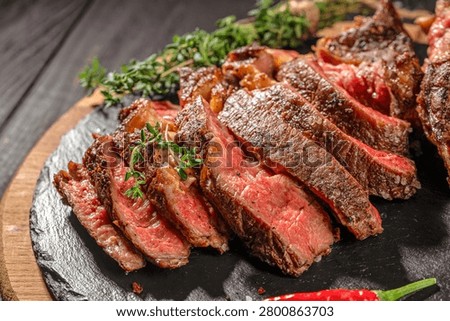 Close up of sliced medium rare tomahawk steak with thyme and sea salt on slate serving board. Juicy grilled beef with visible texture.