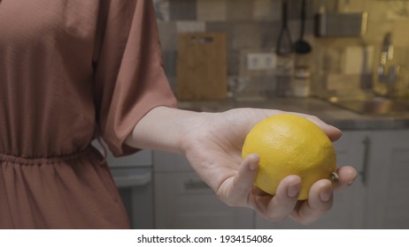 Close up of a slim woman in a brown home dress holding a fresh lemon in her hand. Action. Concept of cooking food at the kitchen at home.