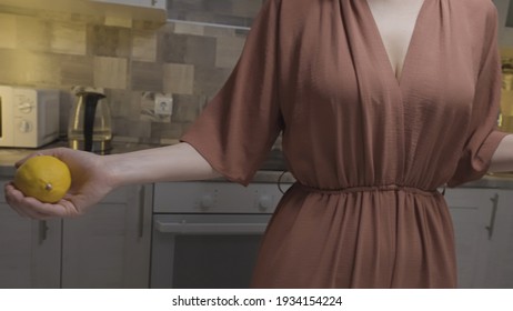Close up of a slim woman in a brown home dress throwing fresh lemon from one hand to another. Action. Concept of cooking food at the kitchen at home.