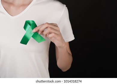 Close up of a slim woman in white t-shirt holding and showing green awareness ribbon in her hands on black background - Shutterstock ID 1014318274