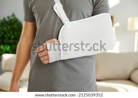 Close up of sling on broken arm of man he needs to wear during rehabilitation period. Unknown male patient wearing immobilizer after car accident or after sports injury. Orthopedics concept.