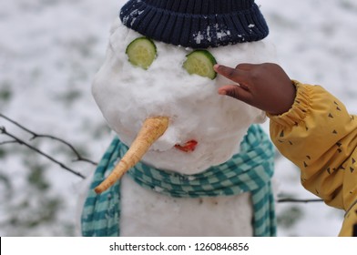 Close Up Of A Small African American Child Putting Cucumber Eyes On A Snow Man