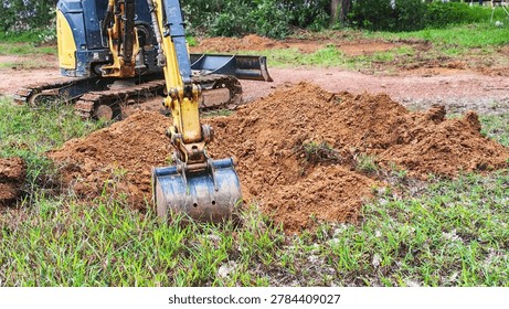 Close up of small backhoe digging earth at a ground works project. Small excavator working on landscaping and moving dirt in a backyard.