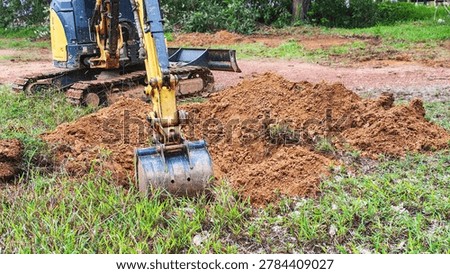 Close up of small backhoe digging earth at a ground works project. Small excavator working on landscaping and moving dirt in a backyard.