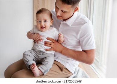 Close Up Small Child Sitting On Dad Lap, Looking At Camera And Smiling. Father Holding Son Baby Boy Indoor