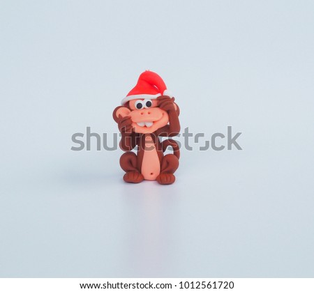 Close up Small cute clay cartoon monkey handmade wear red Christmas hat and naughty funny face to tease on white background for kid , interior garden decoration , green rawmaterial