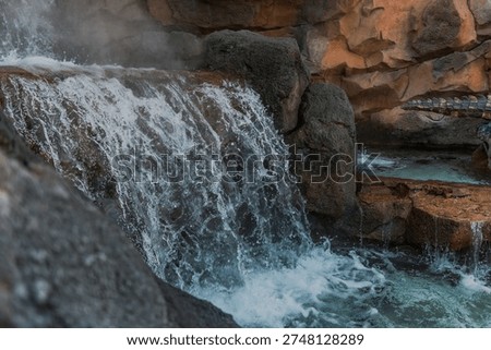 close up of a small man-made waterfall with artificial rocks in the background, taken on a sunny day.