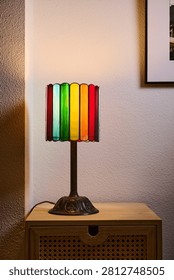 Close up of a small, multicolored table lamp resting on a piece of living room furniture. Colorful lighting and a homey atmosphere.