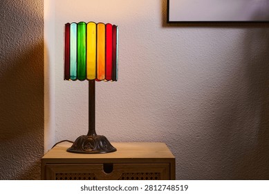 Close up of a small, multicolored table lamp resting on a piece of living room furniture. Colorful lighting and a homey atmosphere.