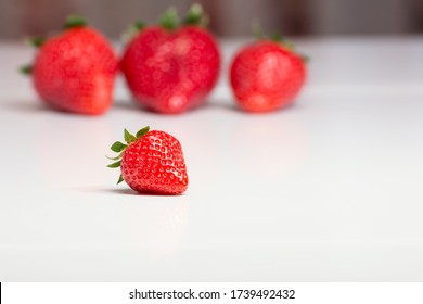 A Close up of a small strawberry and in the blurred background three large strawberries