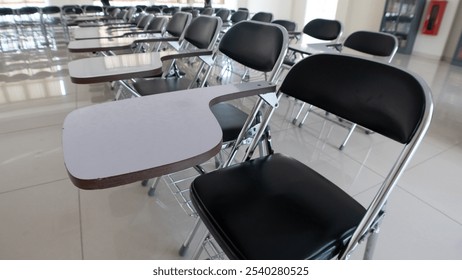 Close up of a small table attached to a student chair. Perspective of the student chairs lined up in a straight line
