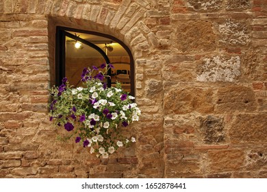 Close up of a small window with blooming petunia flowers in an old antique stone wall in an Italian village.