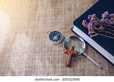 Close up of the small wooden cross on a magnifying glass and a compass and bible with flowers on vintage sack cloth, Christian Background , Focus on Jesus Christian concept with copy space.