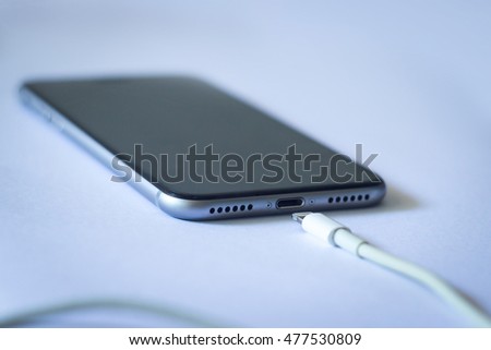 Close up of smartphone charging with white lightning cable on white background. Mobile phone connected to charger power supply. Battery charging process of modern cellphone. Technology and energy concept with copy space for design.