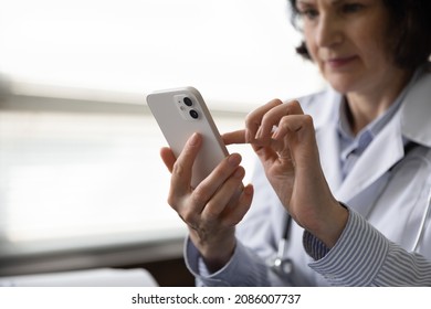Close up of smartphone in female doctor, medic physician hand. Senior general practitioner using virtual online medical app, chatting, texting patients, browsing, consulting internet. Close up
