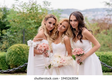 Close of smiled bride, wearing in wedding dress, holding bouquet of roses; standing between bridesmaid and looking at camera