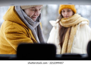 Close Up Of Smiling Adult Man Unloading Car Trunk In Winter While Travelling With Family For Christmas