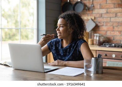 Close up smiling African American young woman recording voice message, sitting at table with laptop, holding phone near mouth, speaking, activating digital assistant, searching in internet