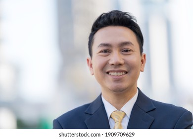 Close up of Smiling asian businessman standing in front of modern office buildings