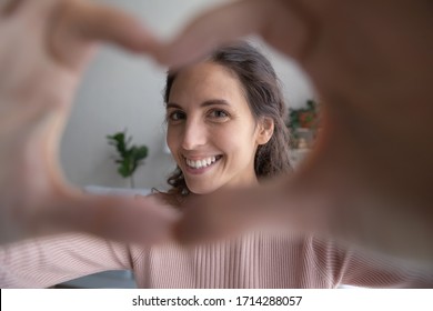 Close Up Smiling Attractive Young Woman Showing Heart Shape Gesture, Looking At Camera. Happy Kind Pretty Millennial Girl Making Love Sign With Fingers, Flirting With Beloved Person Alone At Home.