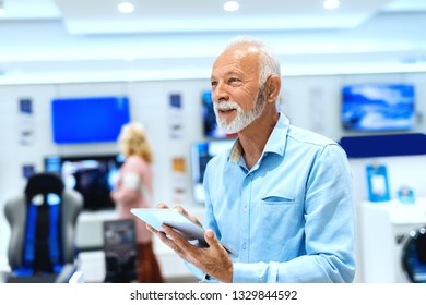 Close Up Of Smiling Bearded Old Man Holding Tablet And Looking Up While Standing In Tech Store.