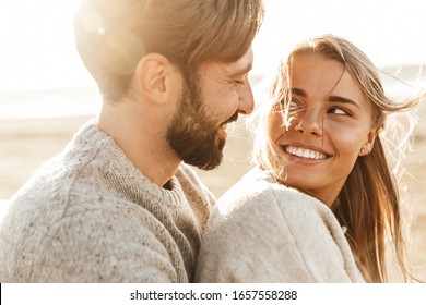 Close up of a smiling beautiful young couple embracing while standing at the beach - Powered by Shutterstock