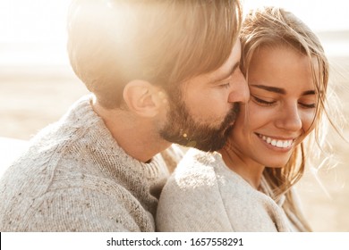 Close up of a smiling beautiful young couple embracing while standing at the beach - Powered by Shutterstock