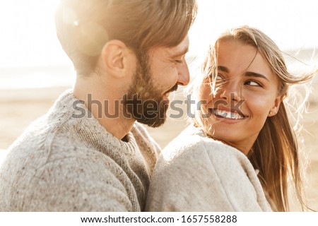 Photo of Close up of a smiling beautiful young couple embracing while standing at the beach