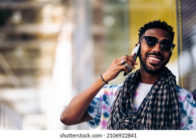 Close Up Of Smiling Black Man Leaning Against A Glass Wall Using His Smartphone