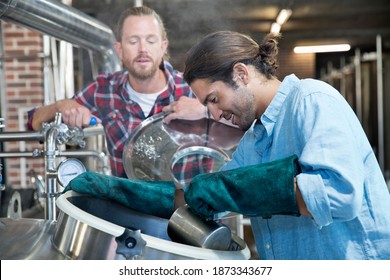 Close Up Of Smiling Brewery Workers Checking Fermentation Process In Steel Vat