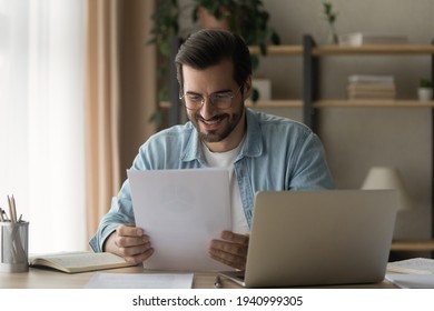 Close up smiling businessman wearing glasses reading good news in paper letter, sitting at work desk with laptop, happy satisfied man holding documents, notification, job promotion, loan approval - Shutterstock ID 1940999305