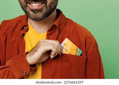 Close up smiling cheerful fun toothy bearded happy man he wears casual clothes t-shirt red shirt hold in hand put mock up of credit bank card in pocket isolated on plain pastel light green background - Shutterstock ID 2276661297