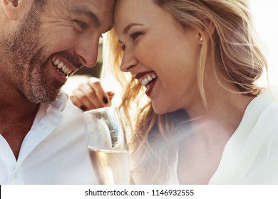 Close up of smiling couple with their heads touching and laughing. Loving couple with wine enjoying each others company. - Powered by Shutterstock