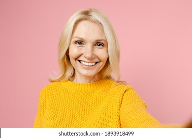 Close Up Of Smiling Elderly Gray-haired Blonde Woman Lady 40s 50s Years Old Wearing Yellow Casual Sweater Doing Selfie Pov Shot On Mobile Phone Isolated On Pastel Pink Color Background Studio Portrait