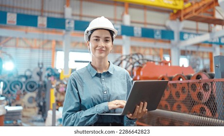 Close up smiling face of engineer manager leader woman wearing helmet holding laptop looking at camera at manufacturing factory - Powered by Shutterstock