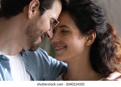 Close up smiling faces of loving young 30s couple. Hispanic woman Caucasian man standing indoor hugging touch foreheads feeling love enjoy tender moment. Romantic relations, newlyweds spouses concept