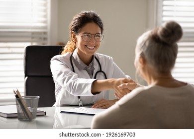 Close up smiling female doctor wearing glasses and uniform with stethoscope shaking mature woman hand at meeting, elderly patient making health insurance deal, older generation healthcare concept