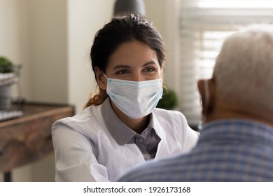 Close up smiling female doctor wearing protective medical face mask listening to mature patient complaints at meeting in hospital, therapist physician consulting senior man, healthcare concept