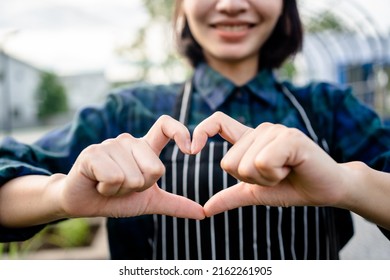 Close up of a smiling female farmer making hands shape heart sign at an organic farm, customer care, service mind, friendliness. - Shutterstock ID 2162261905