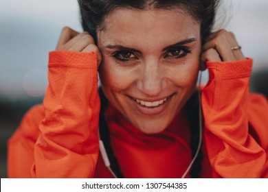 Close up of smiling female runner adjusting her earphones during a workout break. Woman enjoying listening music while having training break outdoors. - Powered by Shutterstock