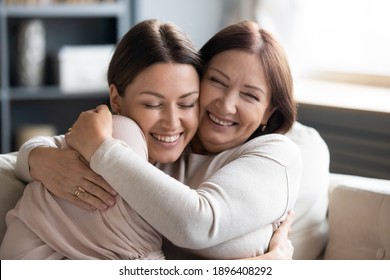 Close up smiling grownup daughter and mature mother cuddling, enjoying tender moment, hugging, expressing love, having fun, sitting on cozy couch at home, family spending leisure time together - Powered by Shutterstock