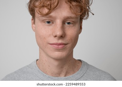 Close up of smiling handsome freckled curly haired ginger teenager model wearing gray t-shirt showing emotions and looking at the camera posing for photo isolated on a grey background in studio shot. - Shutterstock ID 2259489553