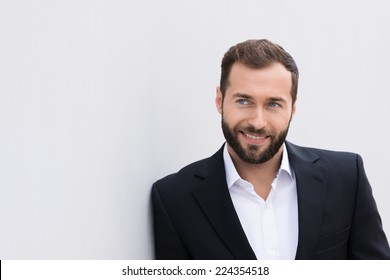 Close Up Smiling Handsome Middle Age Businessman In Black And White Suit Leaning On White Wall.