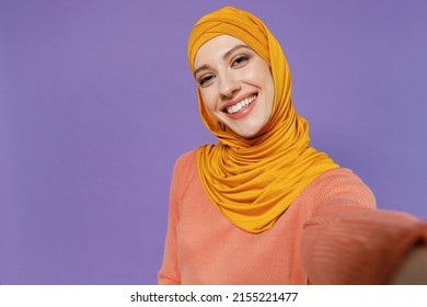 Close Up Smiling Happy Fascinating Young Arabian Asian Muslim Woman In Abaya Hijab Yellow Clothes Do Selfie Shot Pov On Mobile Phone Isolated On Plain Pastel Light Violet Background Studio Portrait